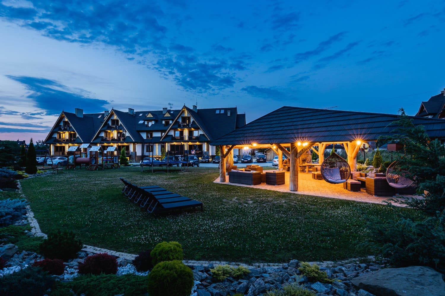 Twilight view of illuminated lodge buildings and covered outdoor pavilion on lawn
