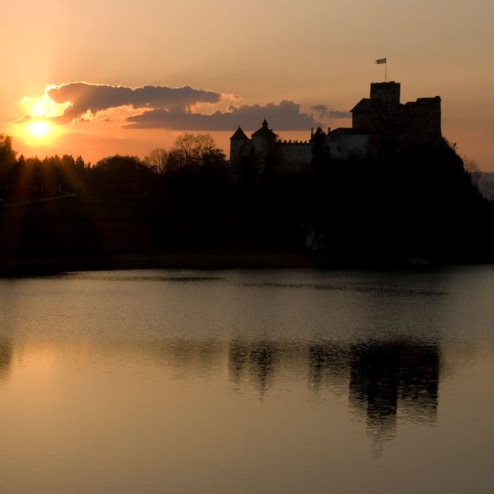 Castle silhouette on a hill at sunset reflected in calm water, warm golden sky